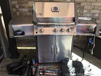 Full front view of stainless steel grill on deck showing hood, cabinet base, side shelves and accessories on ground