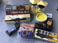 Full lot view showing boxed oscillating power tool, floor installation kit box, door lock kit in packaging, crimping pliers, power inverter, laser level, yellow bowl, and other accessories on gray speckled floor.