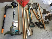 View of assorted garden tools and two metal dog sculptures on a garage floor.