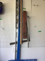 Wide shot showing all items hung on pegboard: wooden carpenter's level, metal torpedo level, blue metal T-square, wooden ruler, metal try square, and socket wrench extension bar.