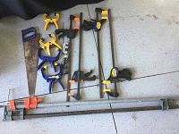 Overall view showing the handsaw, spring clamps, bar clamps, and pipe clamps arranged on the floor.
