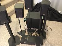 Overview of lot showing 6 Denon satellite speakers, subwoofer, 2 stands, and speaker cables
