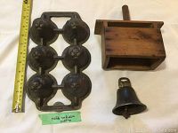 Photo showing the cast iron Yorkshire pudding mould, wooden butter mould, and iron bell with measuring tape for scale.