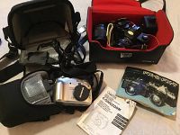 Photo of camera bag, Olympus digital camera with lens and lens cap, charger, and instruction booklets.