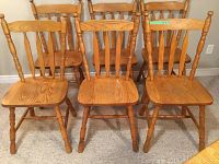 Six oak finish chairs shown from front on carpeted floor