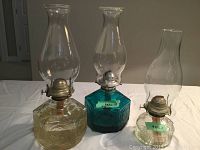 Photo of three vintage glass oil lanterns of two clear and one blue glass bases with chimneys