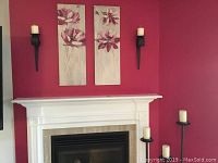 Full view of wall with floral canvas prints, black metal wall sconces with white pillar candles, and 3 tower candle stands with battery-operated candles beside fireplace.