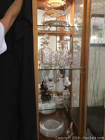 Glass cabinet shelf showing two cut crystal decanters, three finger lamps, and glass plates below