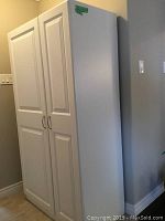 Front view of closed white pantry cabinet showing raised-panel doors and silver handles.