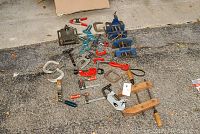 Overview of various vices and clamps arranged on asphalt.