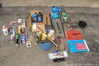 Overall assortment of car accessories and tools arranged outdoors on pavement, showing fluids, tools, brushes, and tool sets.