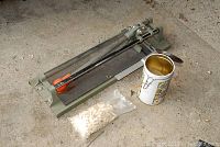 Manual tile cutter with metal rails, black base, and orange-handled sliding cutter on concrete floor.