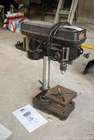 Full view of the JobMate 8" drill press showing motor housing, support column, base, and manual on floor.