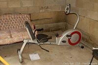 Side view of full recumbent exercise bike with manual on floor and couch in background