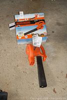 Black+Decker leaf blower with box on concrete floor, showing the assembled unit and packaging.