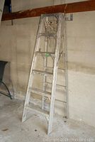 Front view of aluminum folding 6-foot ladder leaning against wall showing overall wear and paint stains.
