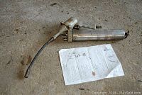 Full view of grease gun with manual laid on floor, showing overall condition and included paperwork.