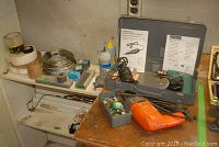 Photo shows assorted tools and hardware on shelves including spools of wire, tape rolls, bottles, and drill cases.