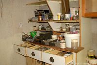 Shelf and drawers with assorted small hardware containers, jars, oils, and miscellaneous parts in a workshop