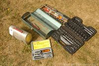 Lot overview showing the two metal toolboxes open on the ground, the black plastic socket set case open, and the metal lunch box-shaped toolbox closed.