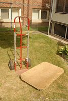 Red metal dolly and beige carpeted creeper placed on grass outdoors