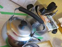 Shows the stainless steel kettle with black handle and knob on lid, sitting next to the pressure cooker.