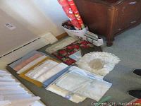 Photo showing folded linen tablecloths, napkins, placemats, and crocheted doilies laid out on the floor
