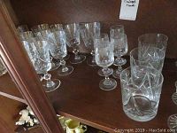Crystal glassware including tumblers, scotch, water, and liqueur glasses on shelf showing cut glass designs.