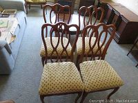 Four wooden dining chairs with curved backs and upholstered seats arranged on a carpeted floor.