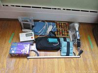 Full view of all items including muscle therapy unit, blood pressure monitors, heating pad, red LED light machine, hand massager, wooden foot roller, ankle weights, and reacher device.