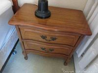 Front view of one wooden night table showing two drawers with ornate metal handles and curved legs.
