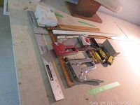 Overview image of assorted staplers, rulers, and measuring tape laid on a surface.