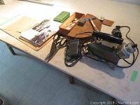 Full view of table showing vintage tailor supplies including iron, foot pedal, scissors, and suit patterns.