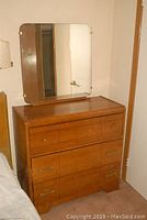 Front view of the wood veneer dresser with three drawers and the attached square mirror with rounded corners.