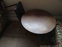 Partial view of folding table with dark wood top showing scuffs and worn finish, placed next to chair.