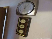 View of both Bulova wall clock and French combo barometer-thermometer-hygrometer unit mounted on wall.