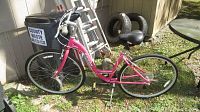 Full side view of pink Dawes woman's bicycle showing frame, tires, seat and handlebars outdoors.