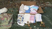 Box with folded linens and towels including pastel and white colors, floral fabric pieces.