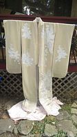 Full view of wedding kimono hung outside showing cream beige color with white floral embroidery on sleeves and front.