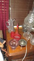 Glass pitcher, red frosted glass pieces and purple tinted bowl on wooden dresser