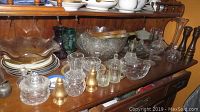 View of tabletop filled with cut glass bowls, pitchers, plates, and containers arranged closely showing a variety of vintage glassware items