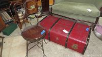 View of red trunk and wrought iron wooden-seat chair together in room setting.