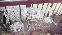 Full bistro set shown on porch including table, two chairs, and plant stand. Table has decorative tile center.