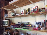 Wide shelf view showing electric crepe maker, Radioshack cordless phones box, auto home wash system box, Sony TV, terracotta planter and other small items on wooden shelves in garage.