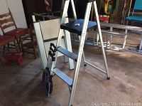 Full view of two step stools side by side in garage space showing aluminum frames and black steps.