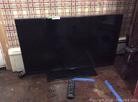 Samsung 32 inch flat screen TV with remote on floor, blue tape marks nearby.
