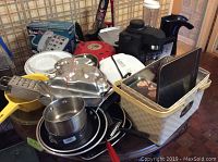 Photo showing various kitchen items including metal pans, dishes, white waffle maker, and basket with kitchen tools on table.