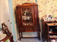 Front view of vintage wood china cabinet with glass door showing interior shelves with decorative crockery inside, standing on four turned legs.