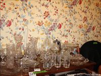 Overall view of various cut glass, crystal and pressed glass items on a wooden shelf with floral wallpaper background.