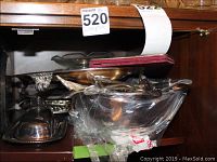 Silver serving dishes and bowls displayed inside cabinet, including covered butter dish and metal platter